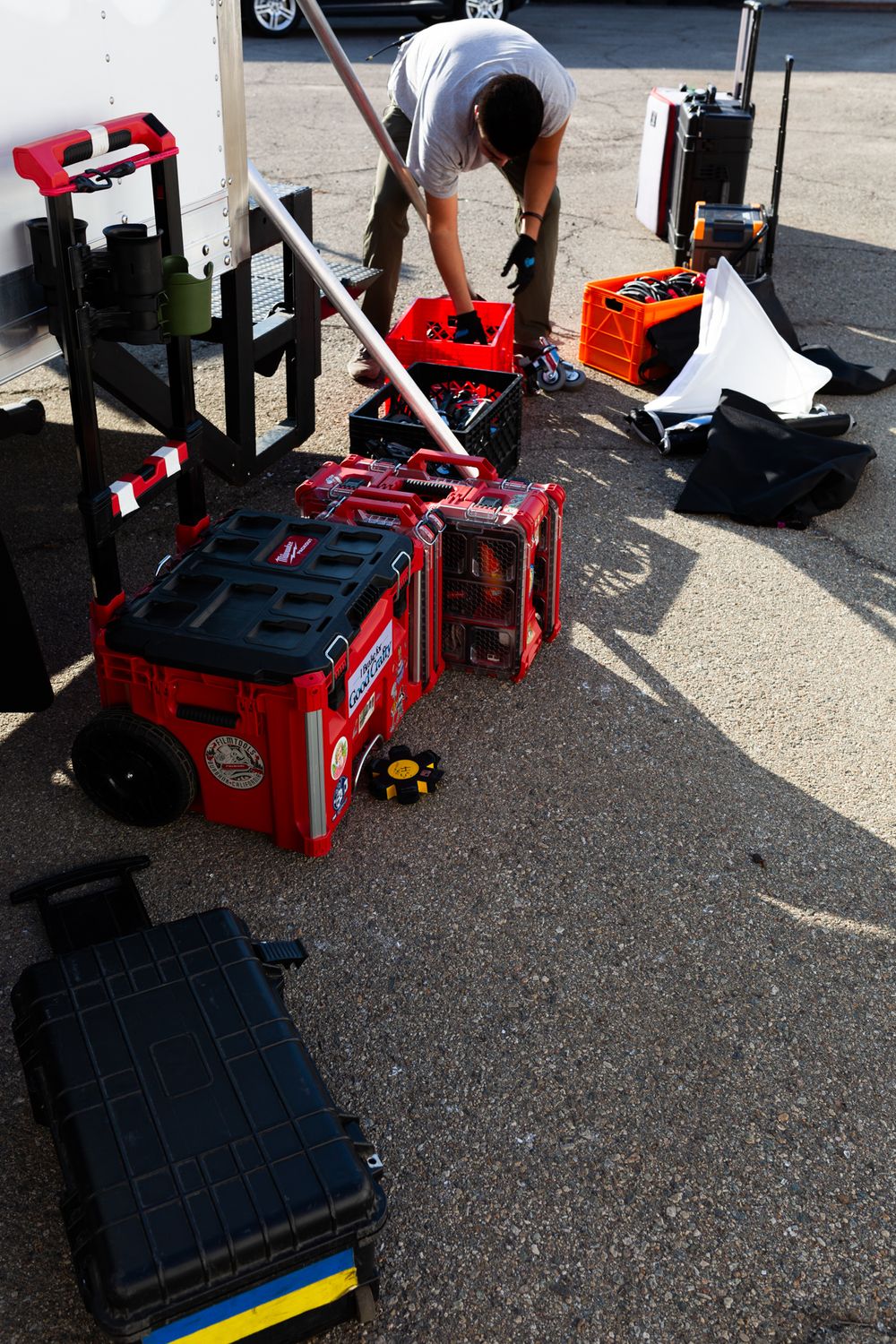 Person organizing red equipment cases and production gear on concrete ground.