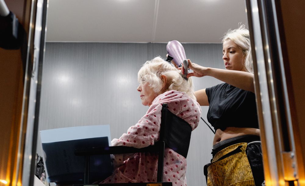 Hairstyling session captured in mirror reflection showing work in progress.