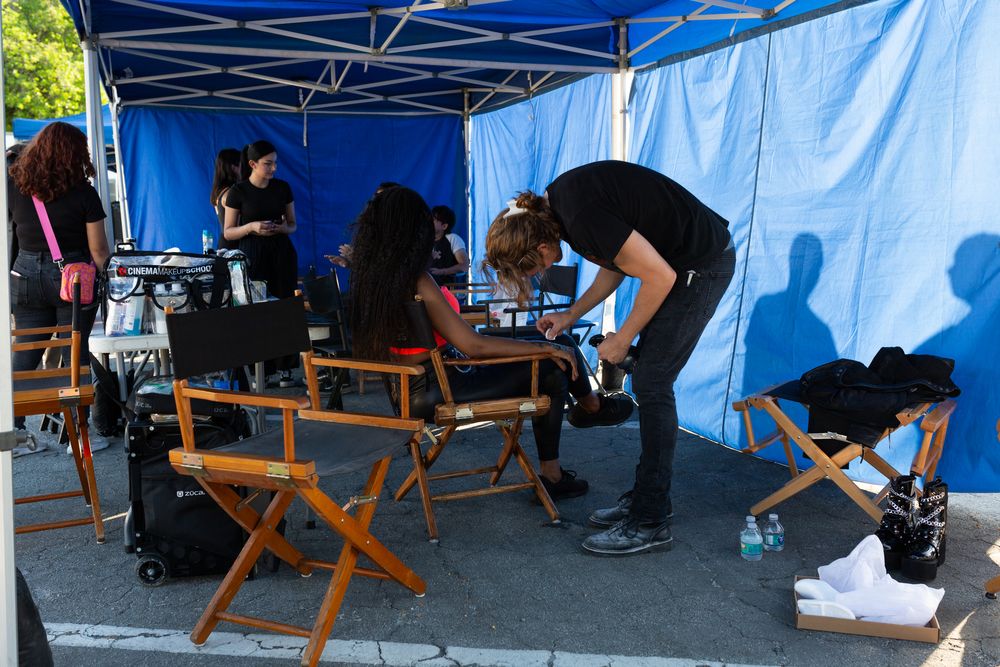 Film crew working under a blue canopy tent with director chairs and equipment.
