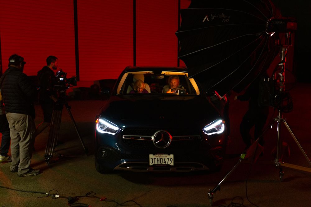 Black Mercedes car with bright headlights being filmed on a dark set with red lighting.