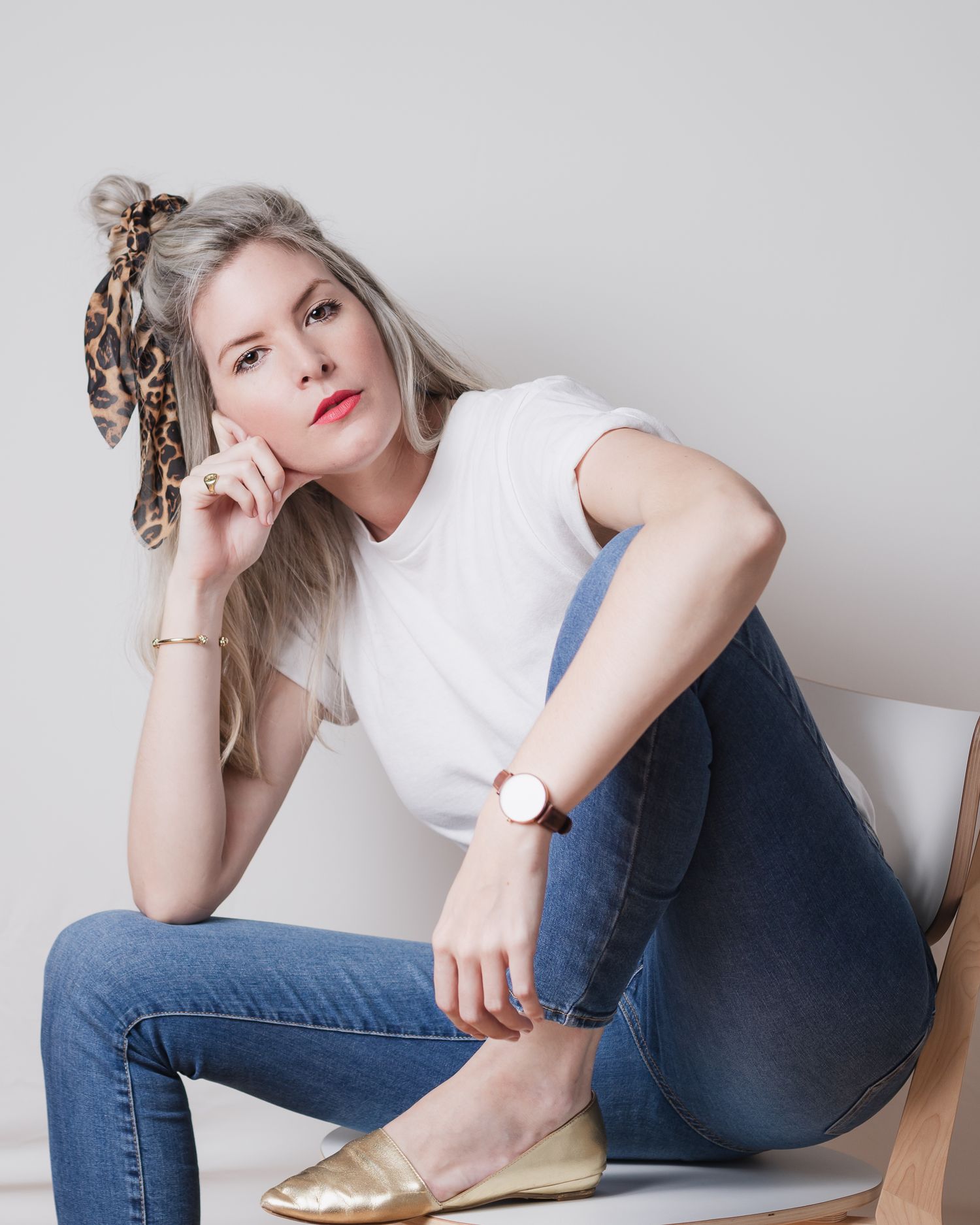 Casual portrait of someone in white top and jeans sitting on chair.