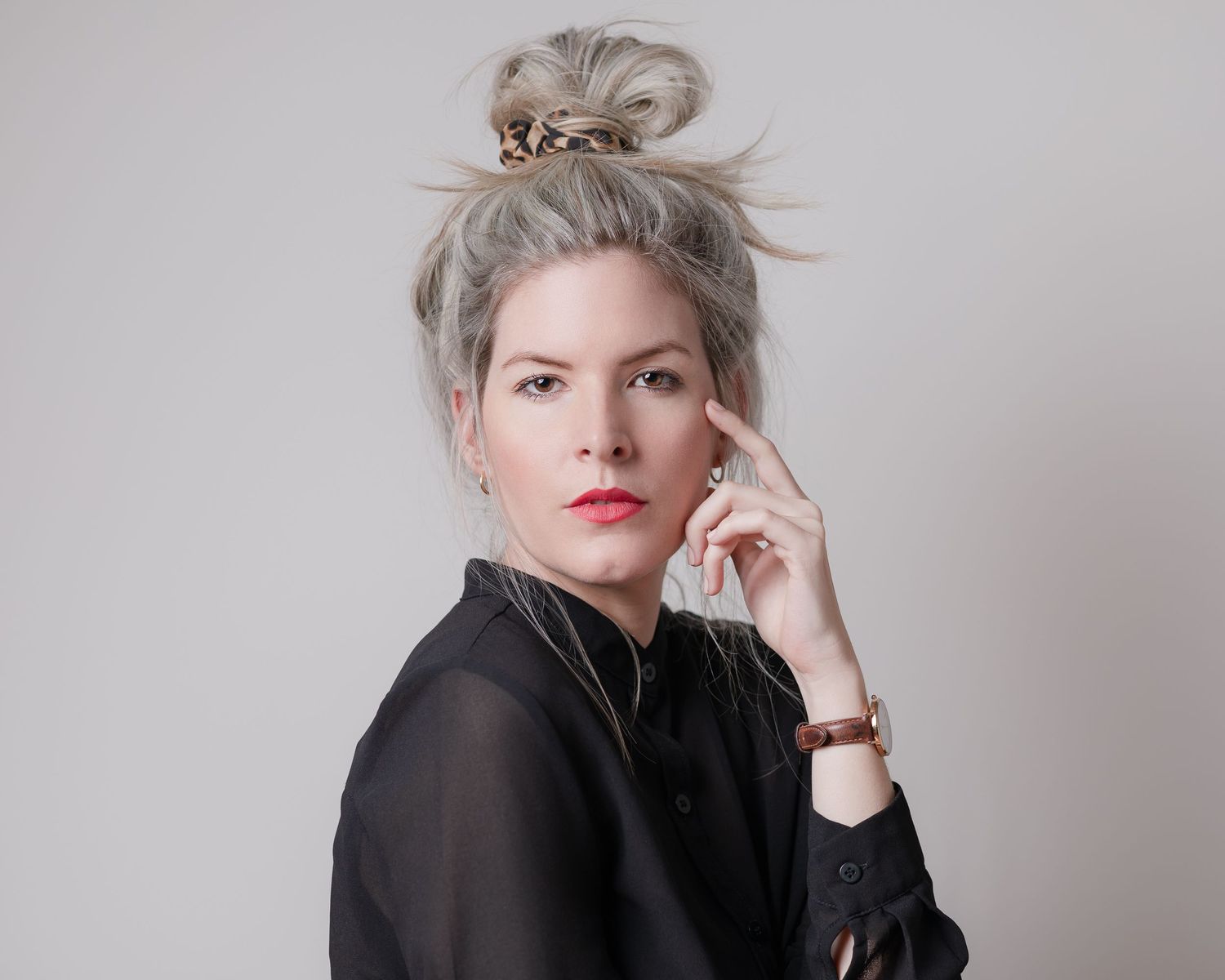 Stylish portrait of someone with blonde updo wearing black top against grey backdrop.