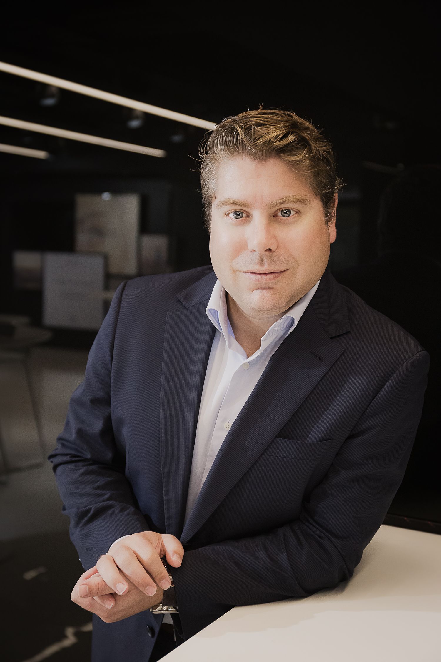 Corporate headshot of a professional in navy suit jacket against dark background.