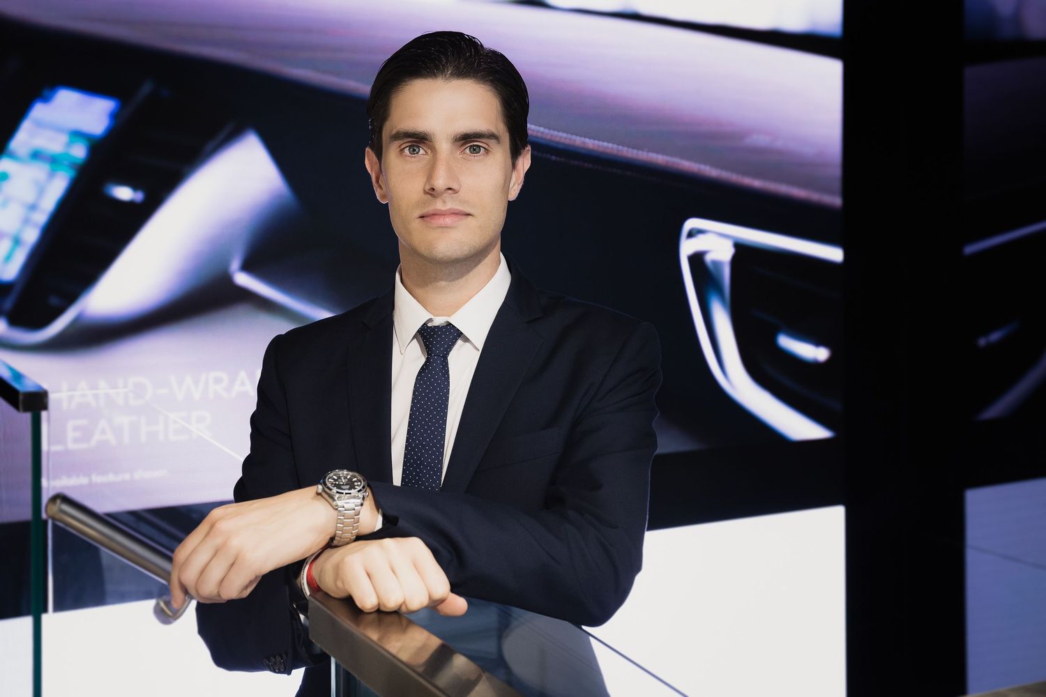 Professional portrait of someone in dark suit checking watch against modern backdrop.