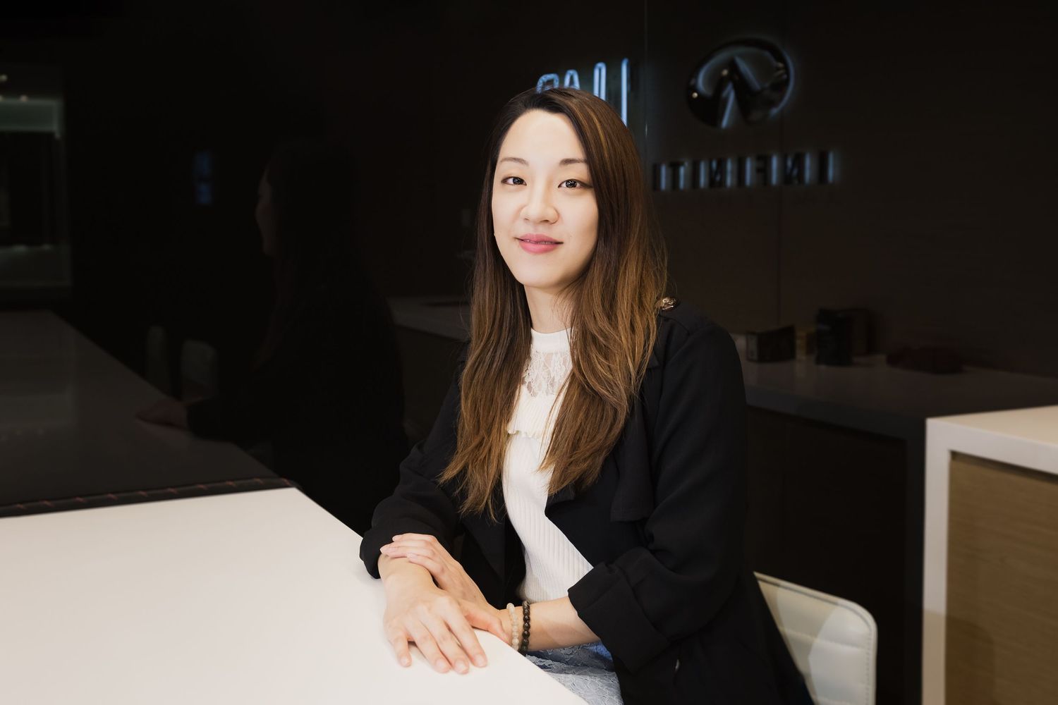 Business professional portrait of someone in black blazer sitting at office desk.