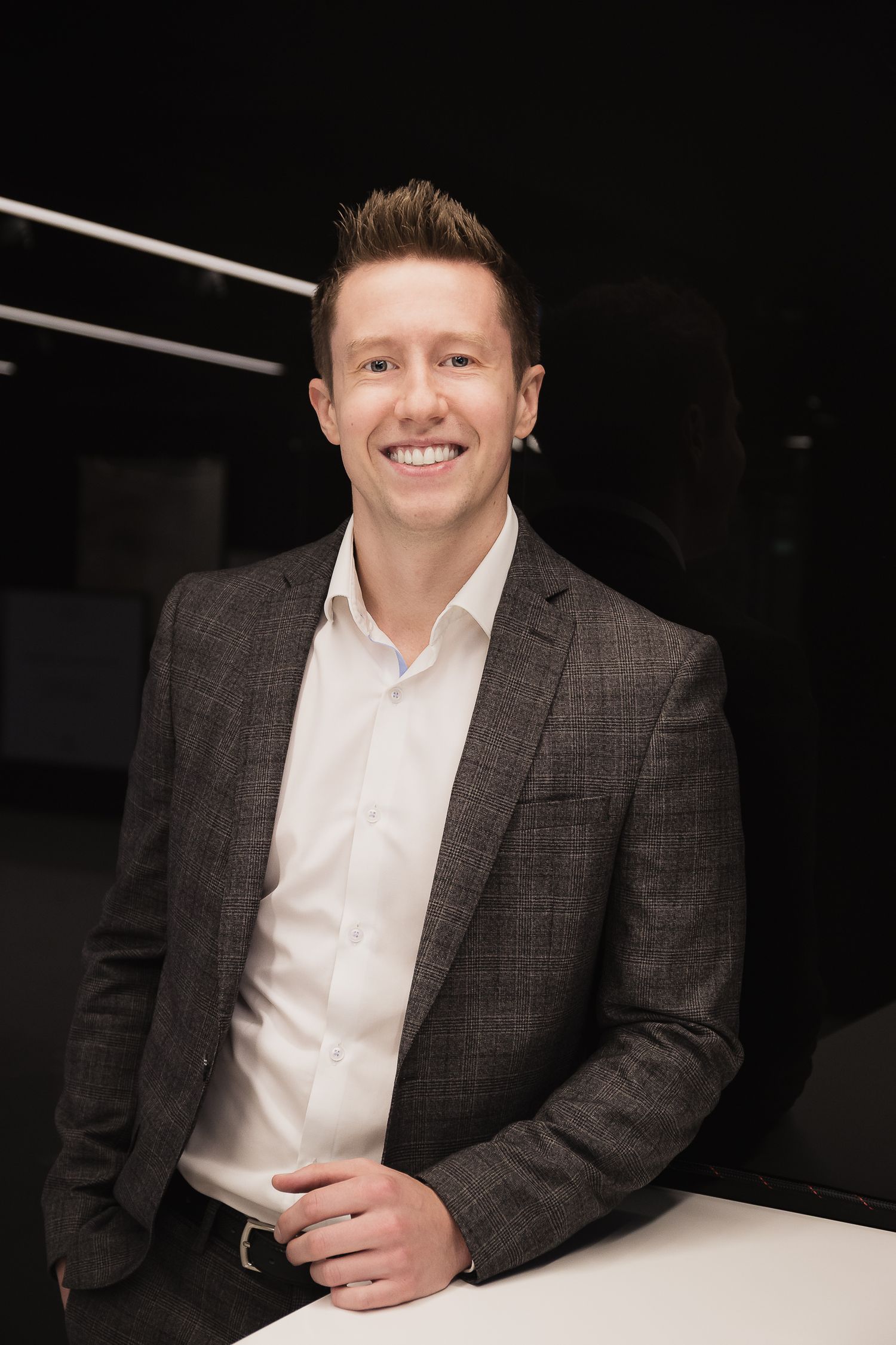 Professional headshot of someone in plaid blazer against dark background.