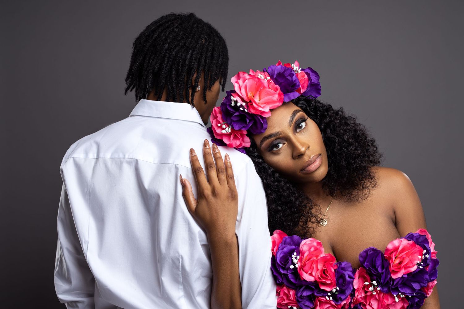 Romantic maternity photo with woman in floral dress and man in white shirt against dark background.