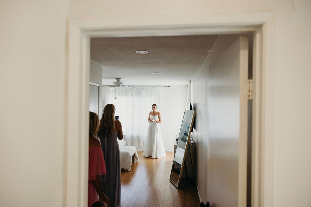 A wedding preparation scene viewed through a doorway in a bright interior space.