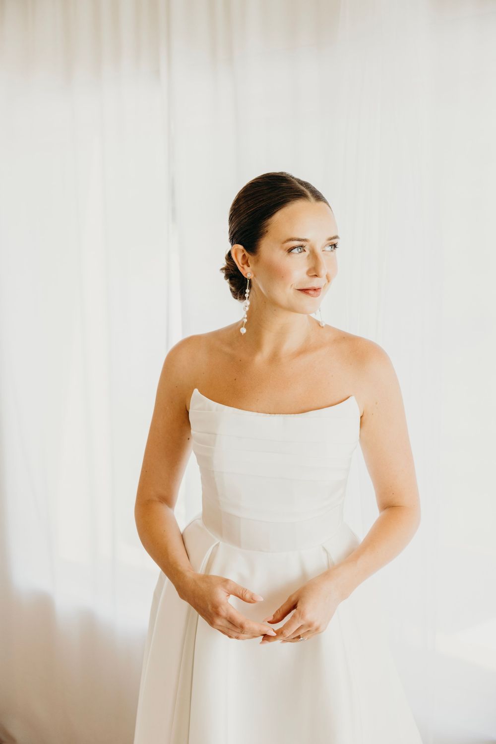 An elegant bride in a strapless white gown poses against a light backdrop.
