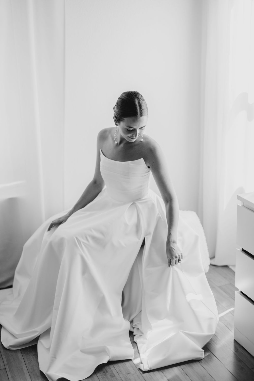 A black and white portrait of a bride adjusting her flowing wedding gown.