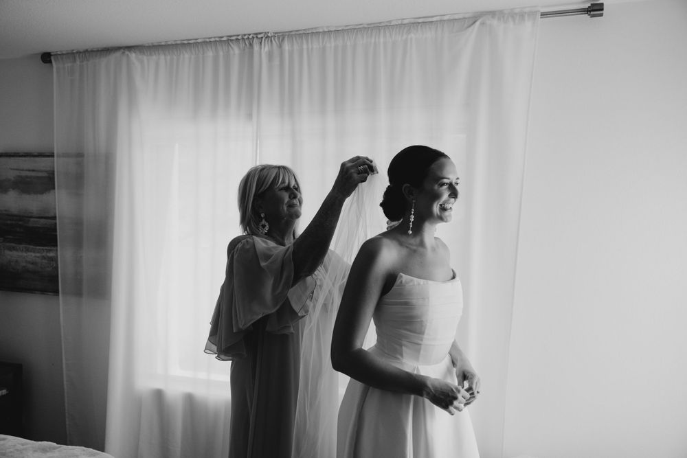 A black and white photo capturing final preparations before a wedding ceremony in a sunlit room.