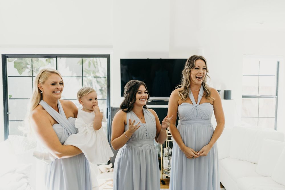 A group wearing light blue bridesmaid dresses gather in a bright white room.
