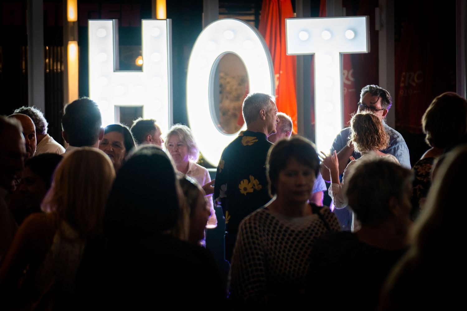 Crowd of people at an indoor event with bright backlighting creating silhouettes.