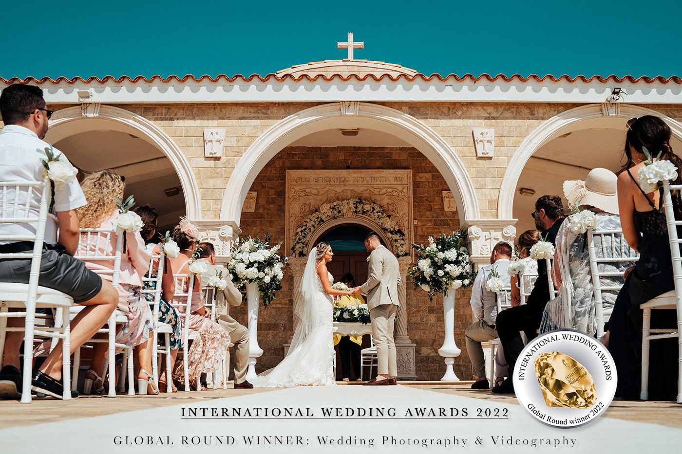 Wedding ceremony in Mediterranean-style church with cross and floral arrangements.