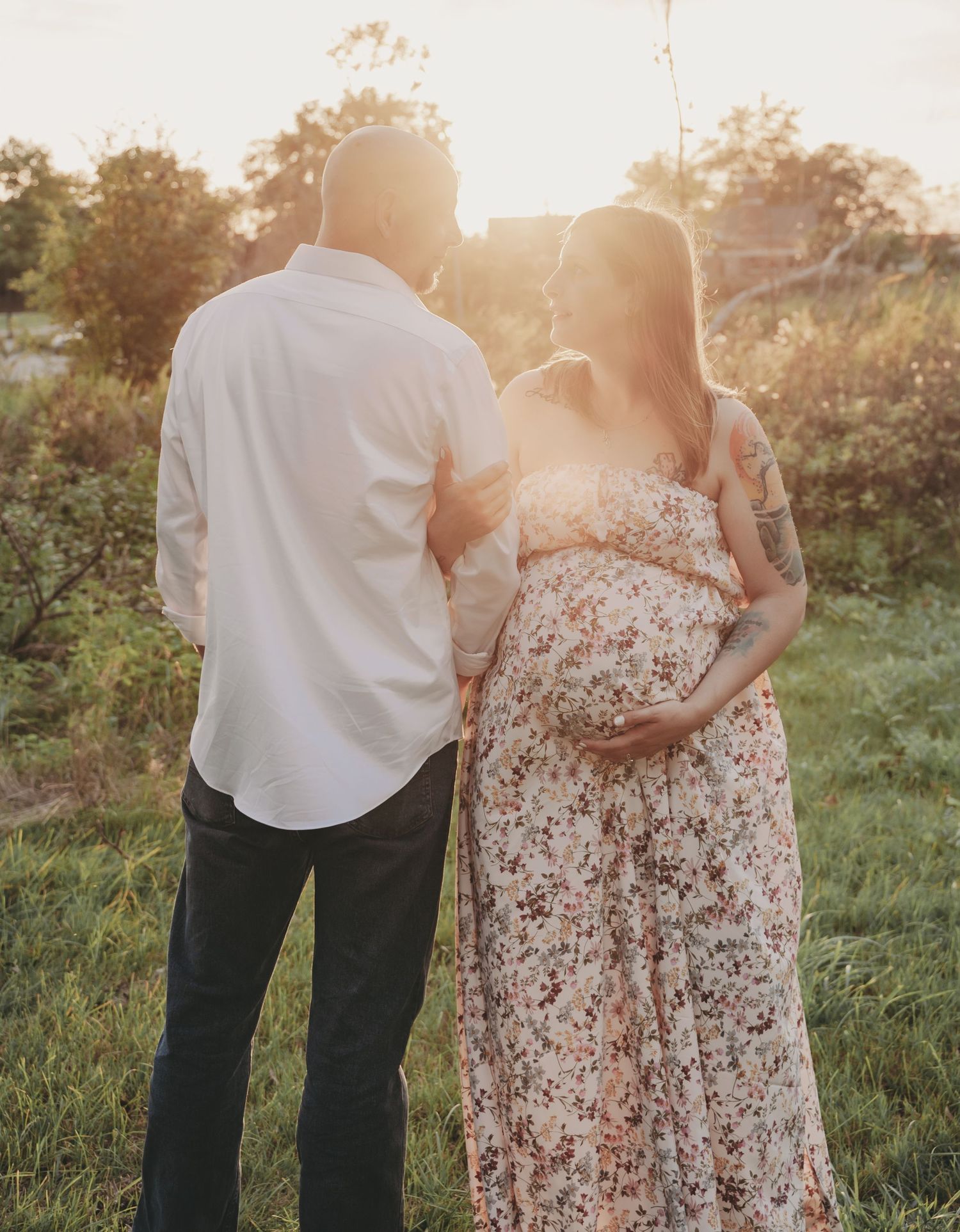 Expectant couple embracing in a sunlit field during golden hour maternity photoshoot.