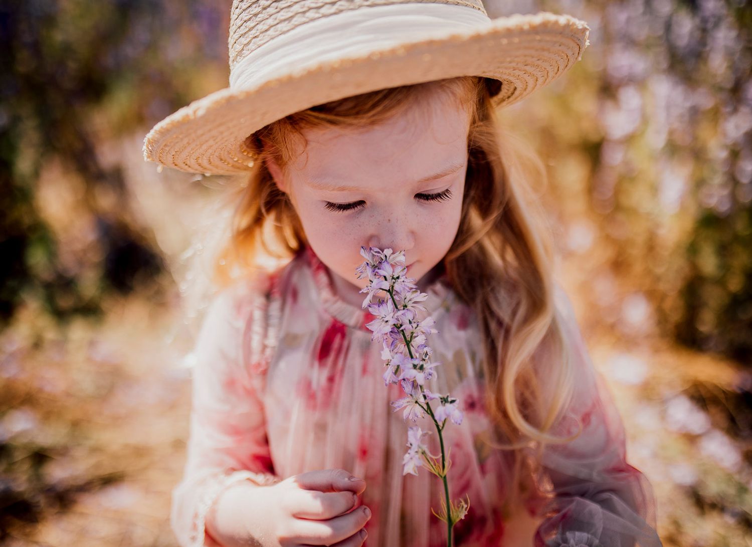 Young child in a sun hat smelling delicate flowers in warm sunlight. Worcestershire Wedding photographer.