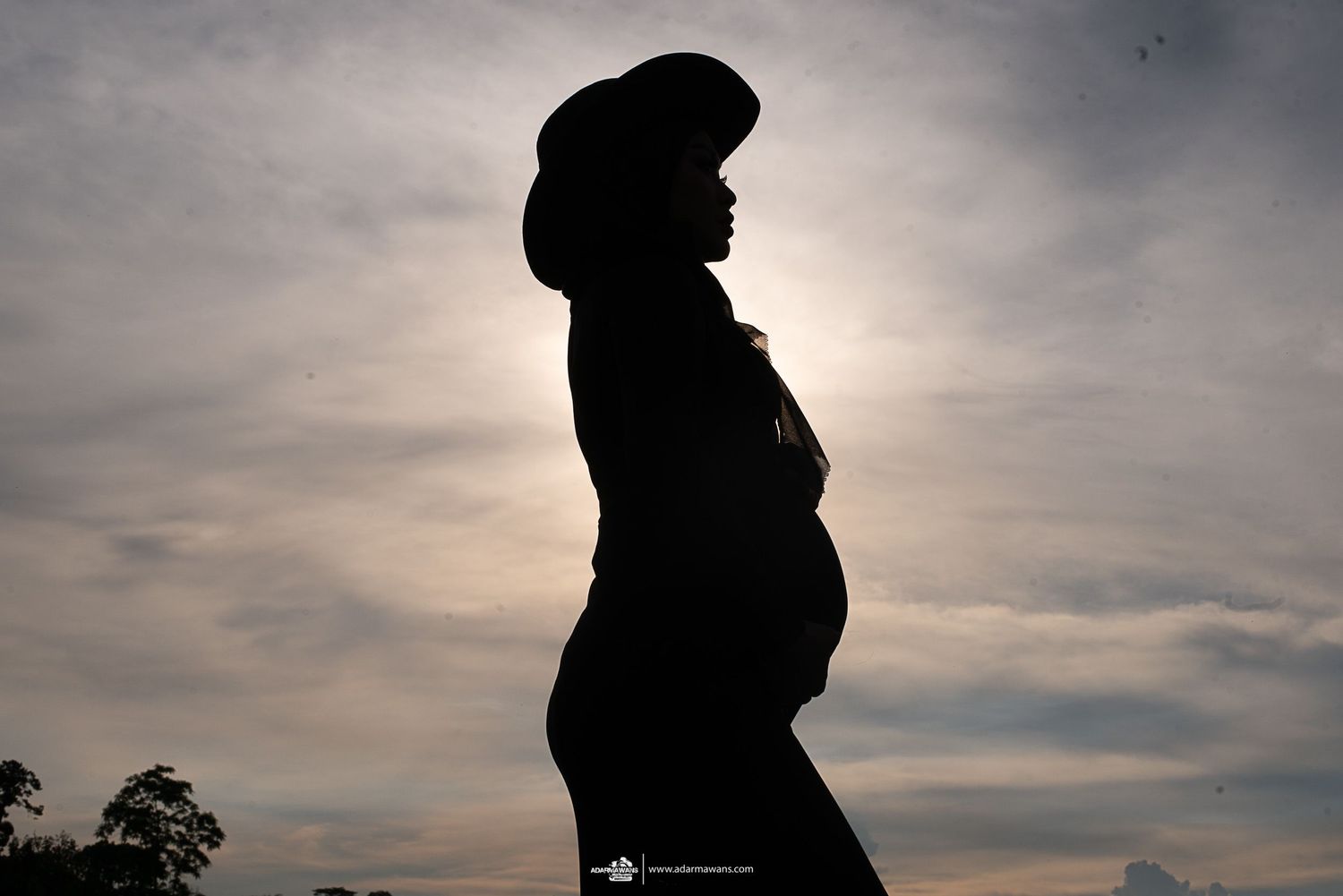 Silhouette of pregnant woman standing against dramatic sunset sky.