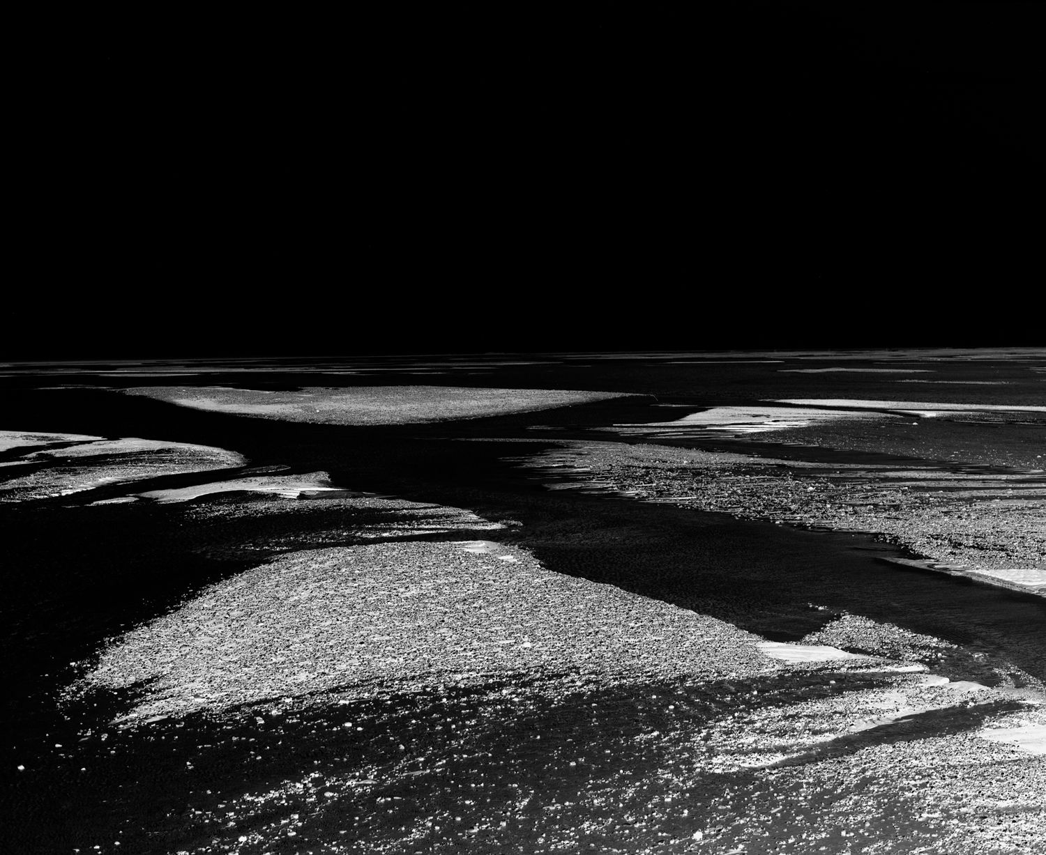 Stark black and white landscape with dramatic shadows and textured terrain patterns.