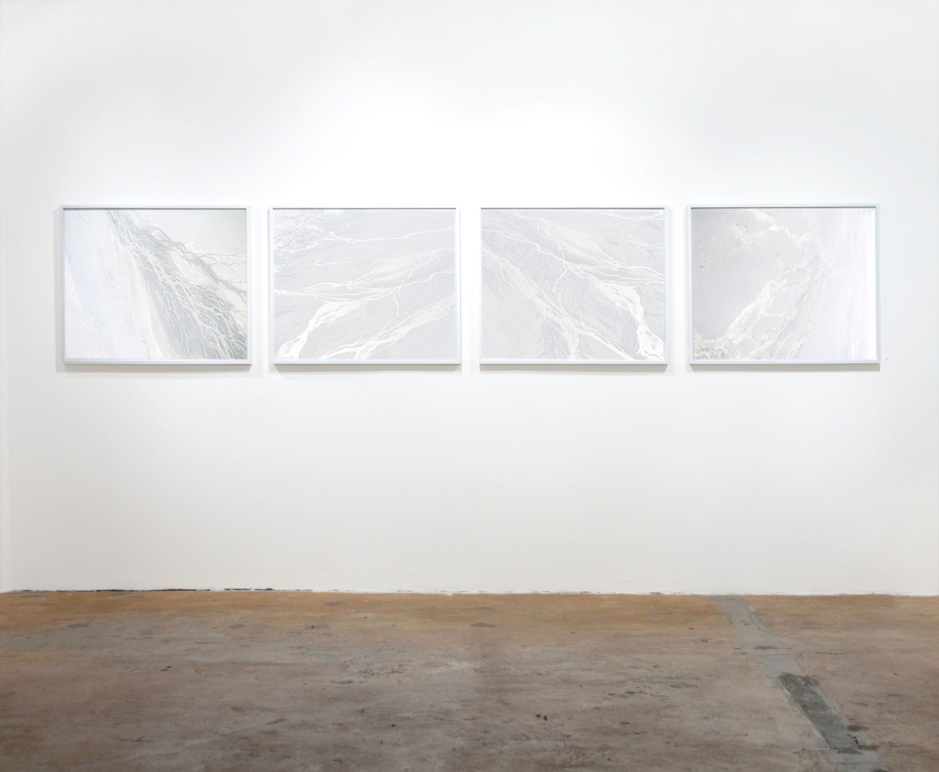 Gallery installation featuring four white minimalist artworks mounted on a plain wall.