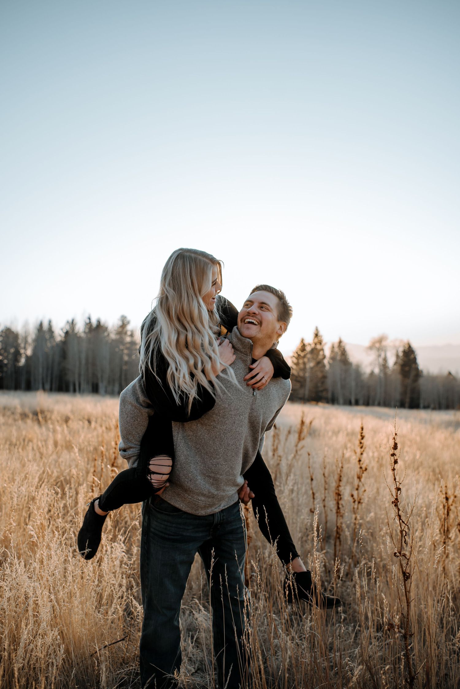 Playful couple laughing together in tall autumn grass during golden hour.