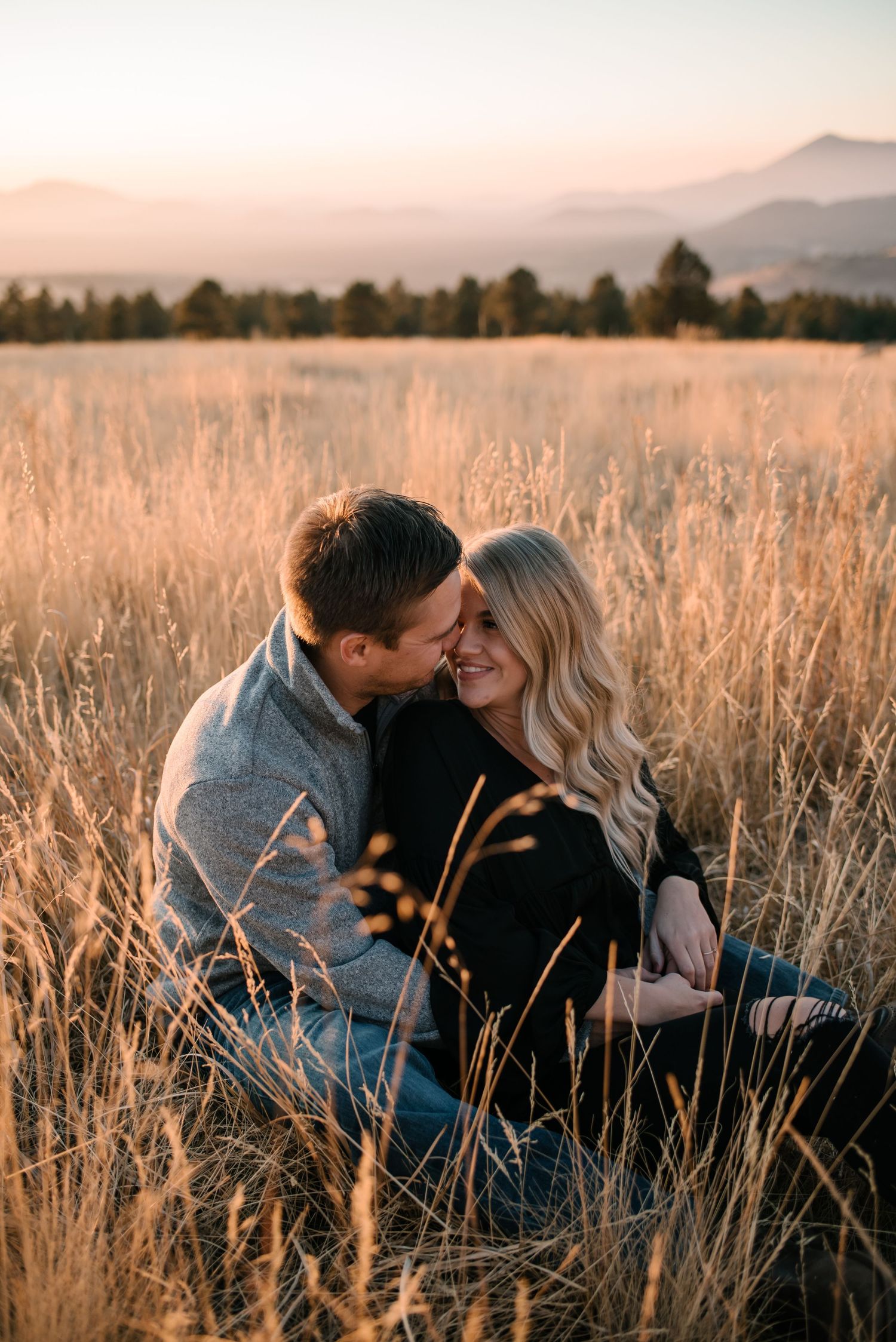 Intimate couple embracing in tall grass field during sunset.