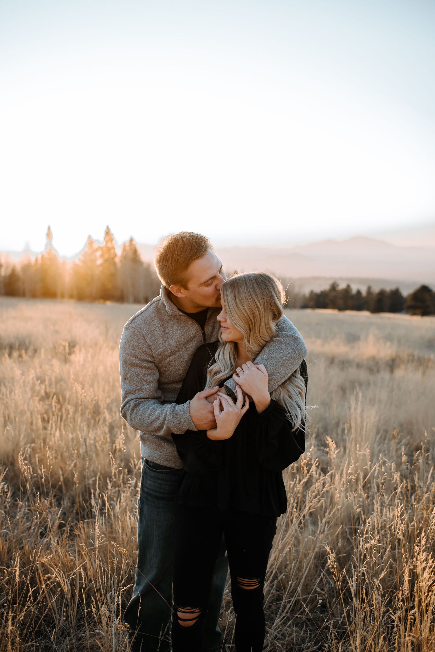 Couple embracing and laughing in autumn field during sunset.