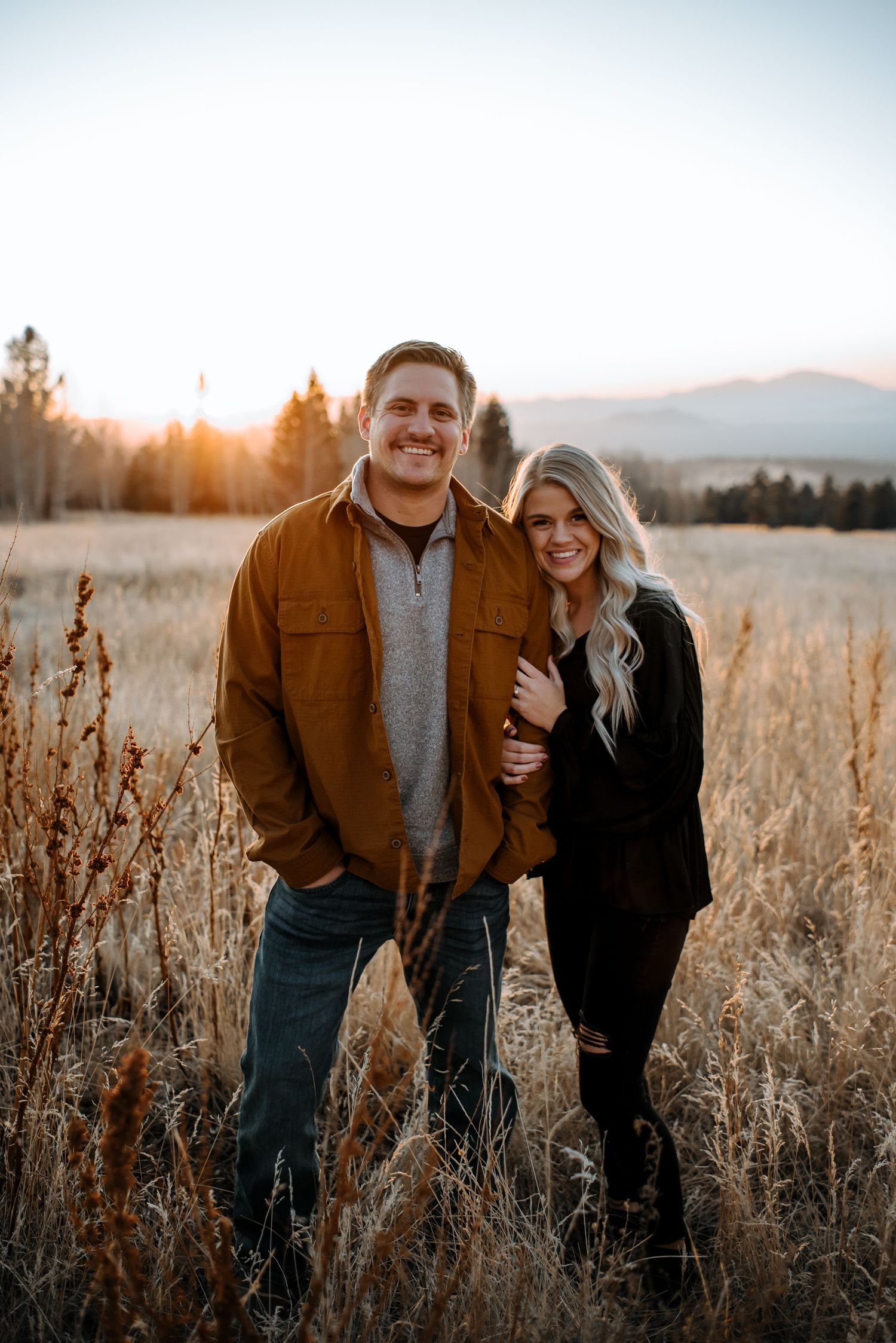Couple in casual attire embracing in golden field at sunset.