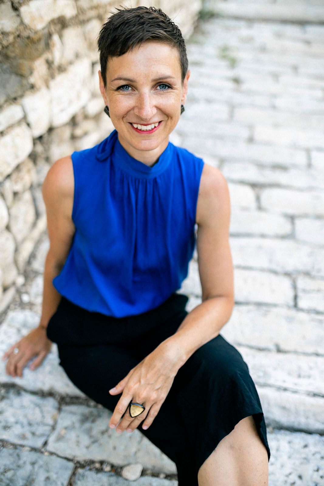 Professional portrait of a person in a blue sleeveless top sitting on stone steps.