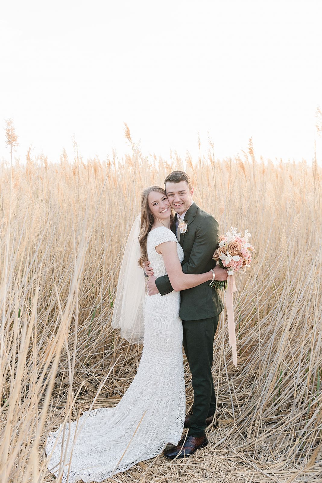 Wedding portrait in golden wheat field with soft sunset lighting and flowing veil.