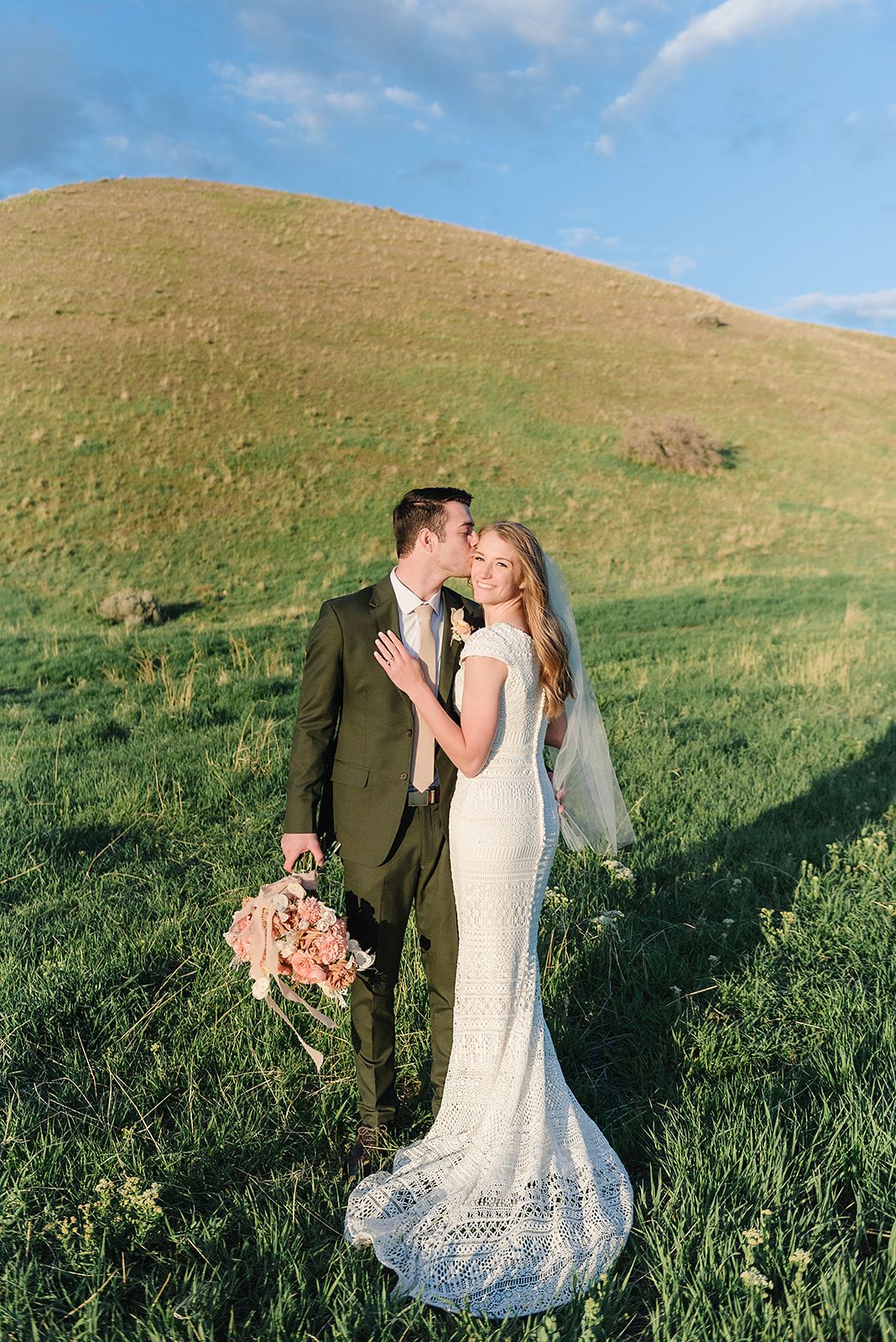 A romantic wedding portrait on a green hillside during golden hour.
