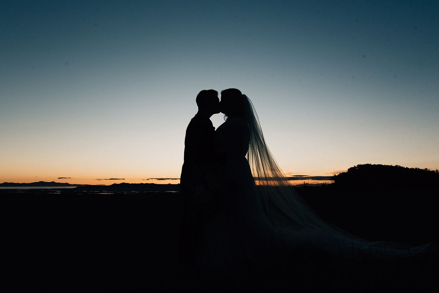A silhouetted wedding couple against a sunset sky.
