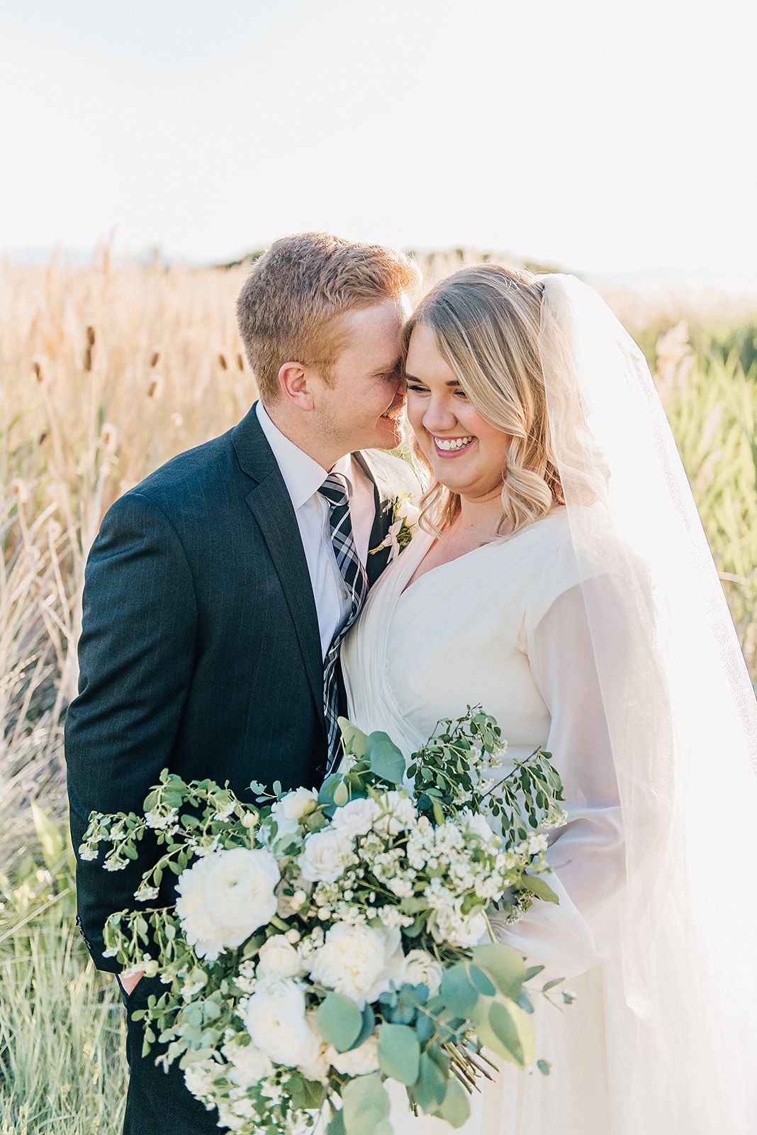 A romantic wedding portrait in a field of tall grass during sunset.