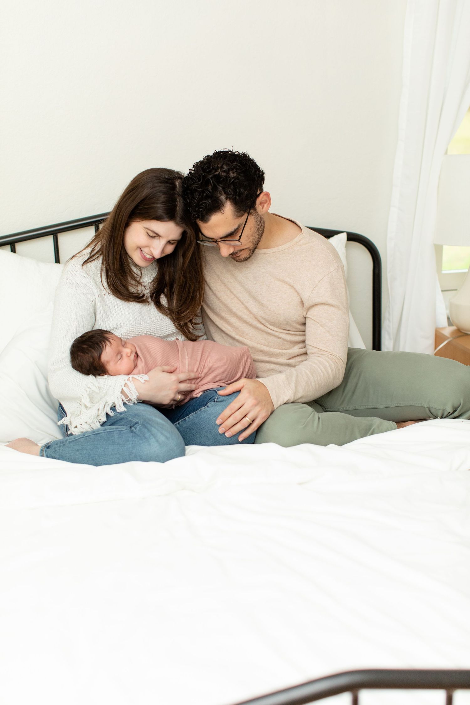 Family shares an intimate moment with their newborn baby while sitting on bed.