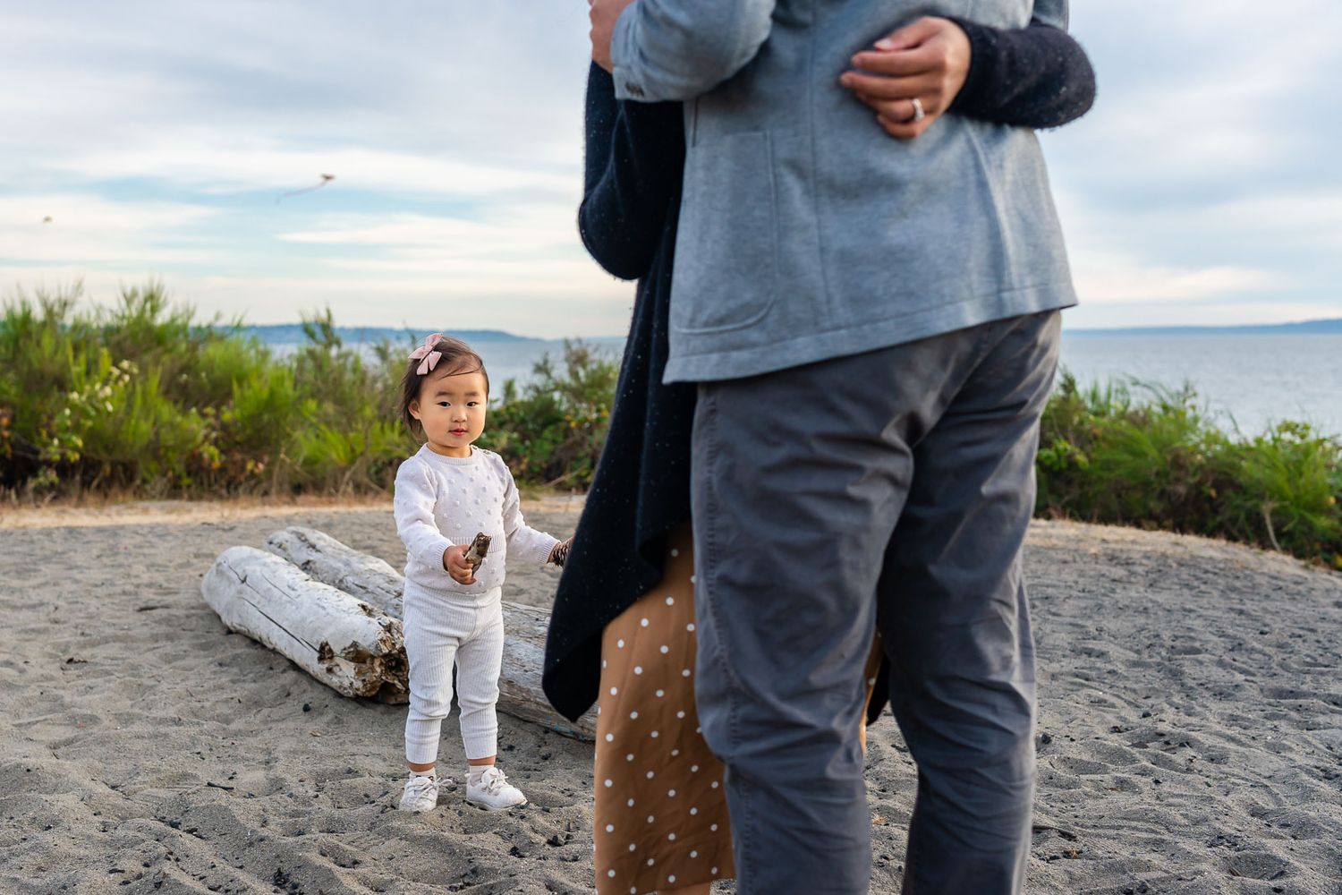 Daughter plays while parents cuddle at the beach.