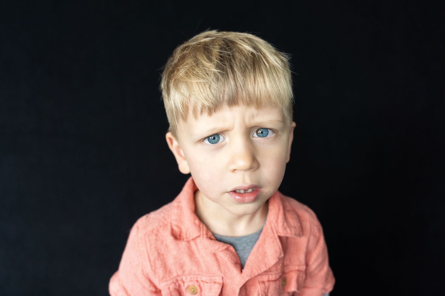Portrait of a child in a coral colored shirt against a dark background.