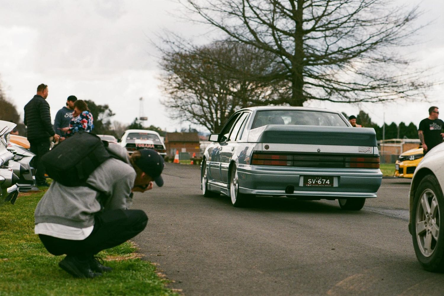 Photographer crouching to capture a white vintage car in a parking lot during daytime.