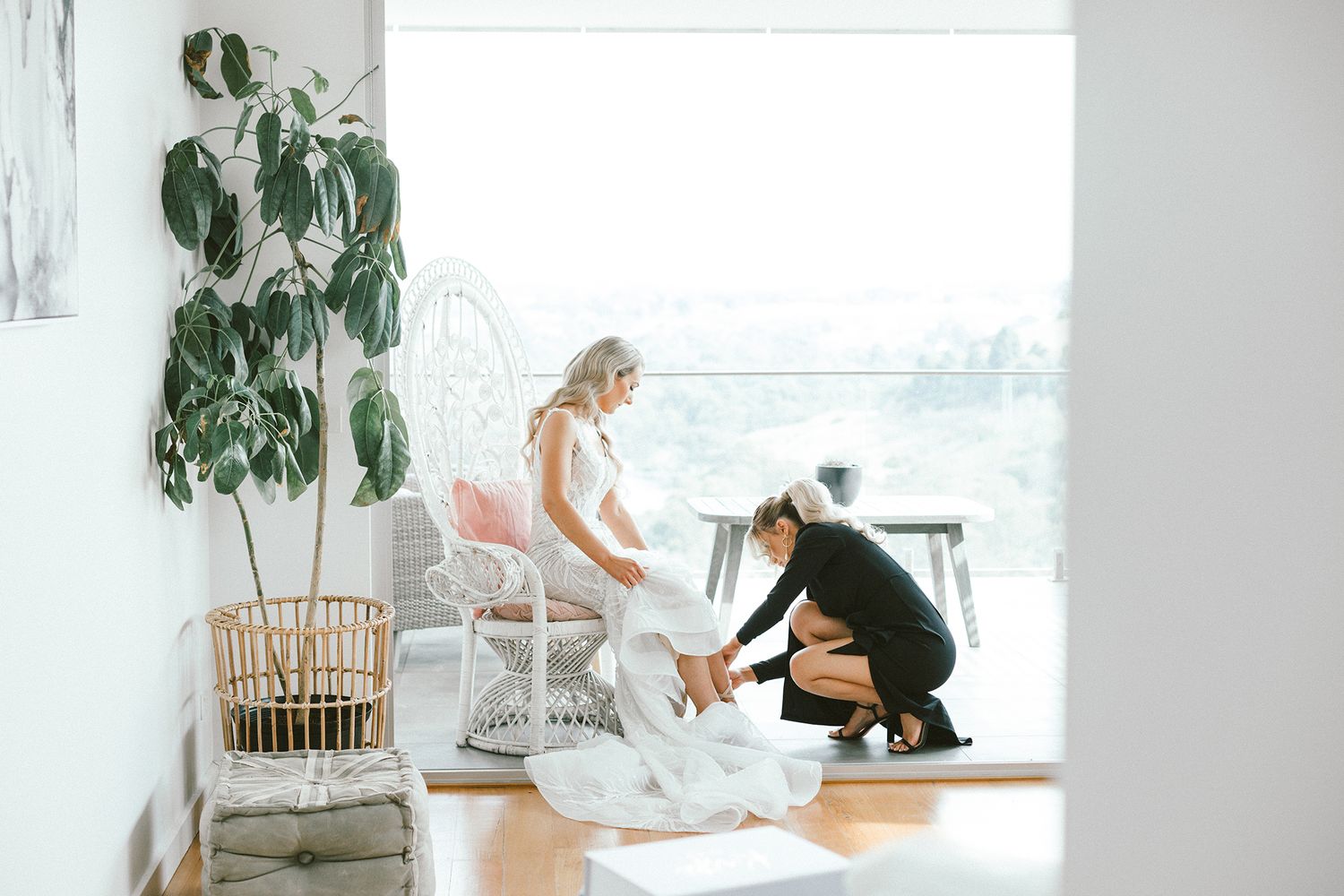 Wedding dress preparations taking place in a bright sunlit room with tropical plants.