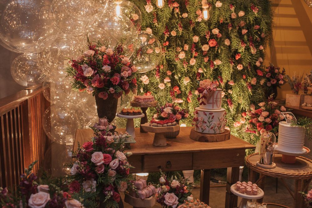 Romantic wedding dessert table decorated with pink roses and twinkling lights under a lush floral canopy.