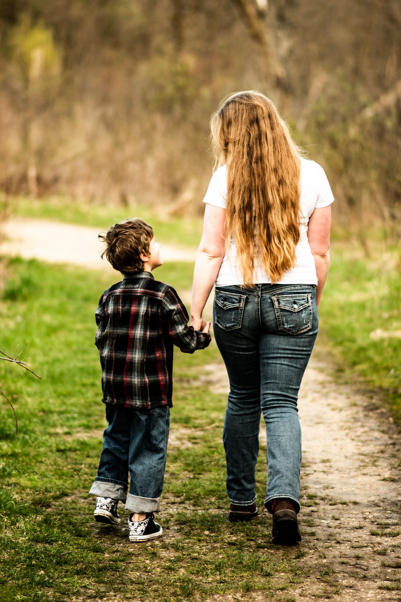 A parent and child walking hand in hand down a nature path.