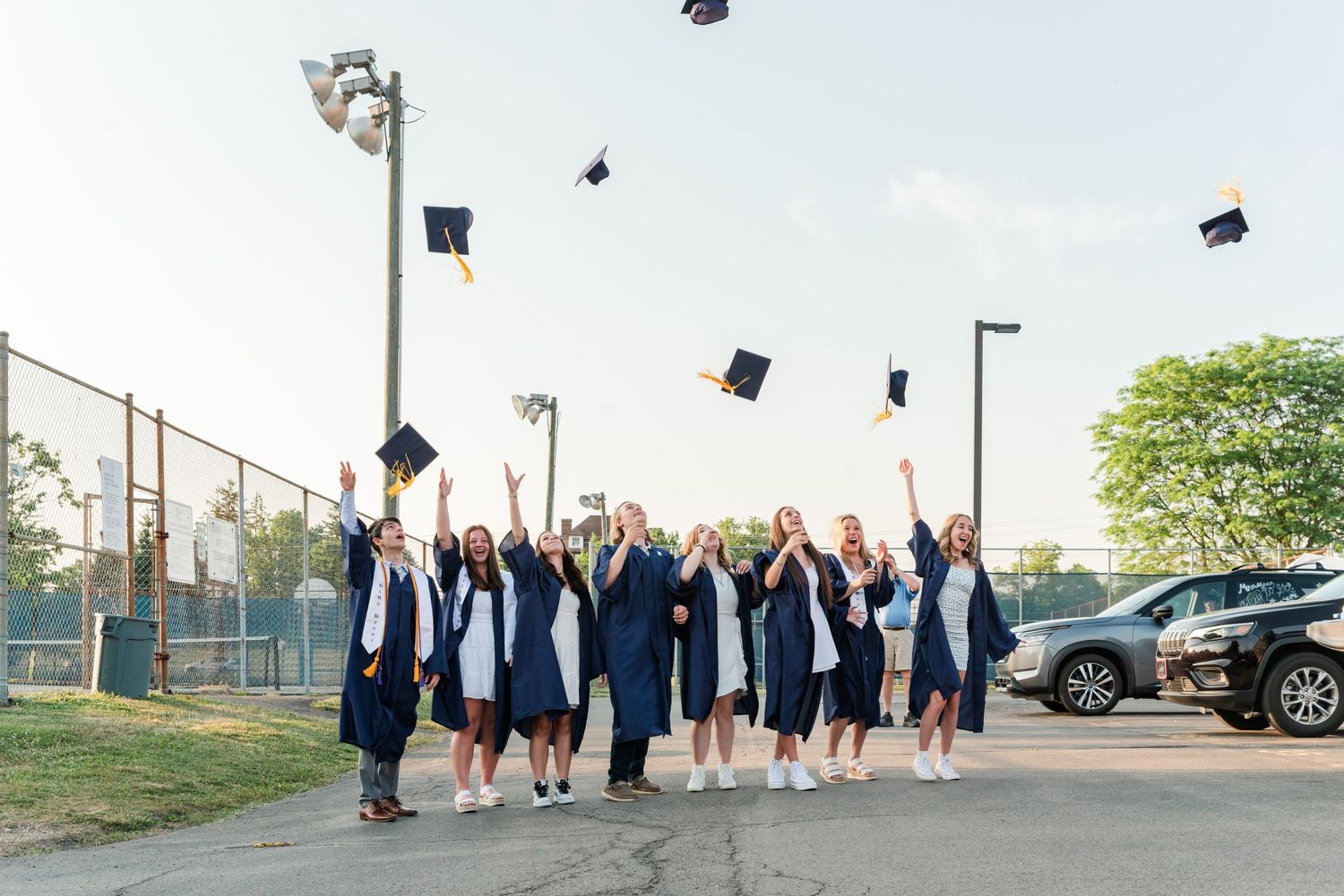 Graduates in blue caps and gowns toss their mortarboards into the air during commencement.