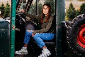 Young woman in casual wear sitting in vintage green tractor cab.