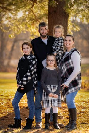 Family wearing coordinated black and white plaid outfits poses together for autumn portrait under golden leaves.