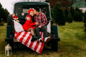 Family sitting in vintage truck with holiday decorations and blanket.