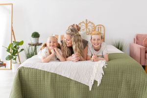 Family lifestyle moment captured on green bedding with white throw blanket.