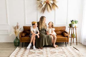 Family portrait on brown leather couch with boho dried floral wall decor.