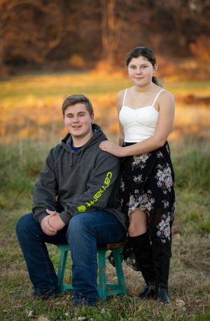Couple poses for outdoor portrait at golden hour with one seated on a teal stool.