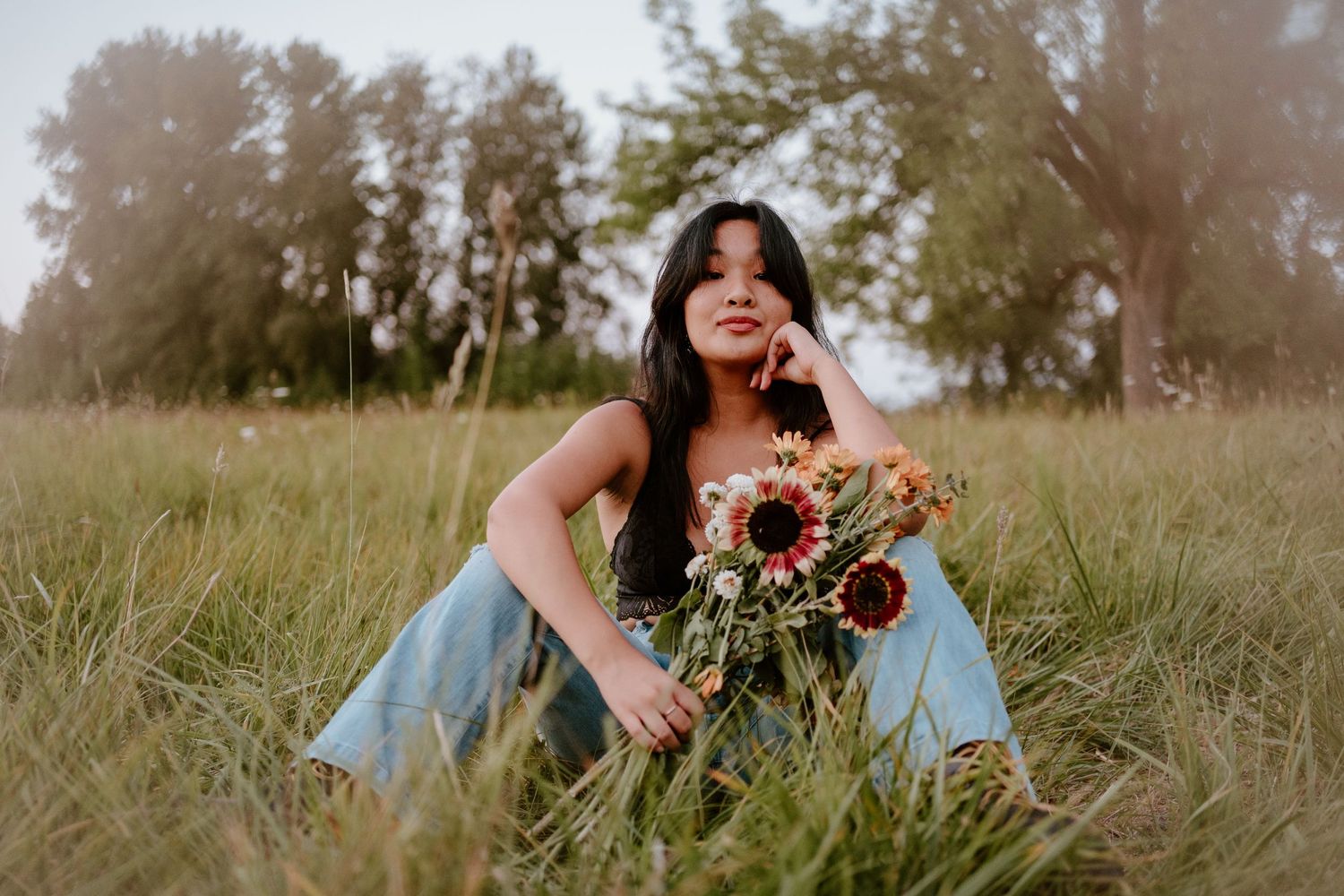 Woman sitting in a summer field holding sunflowers during golden hour.