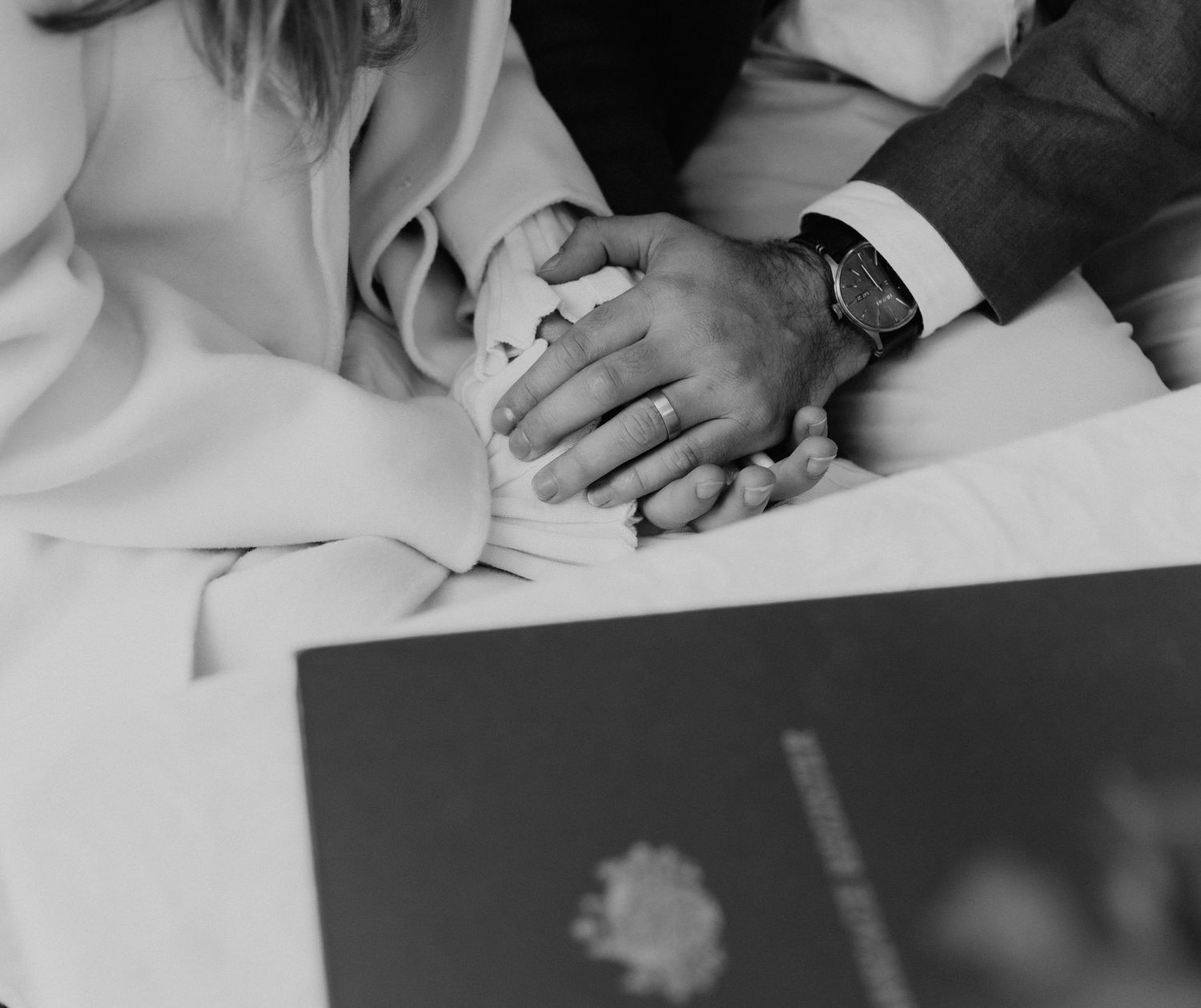 Wedding rings and hands delicately placed on a white surface in black and white.