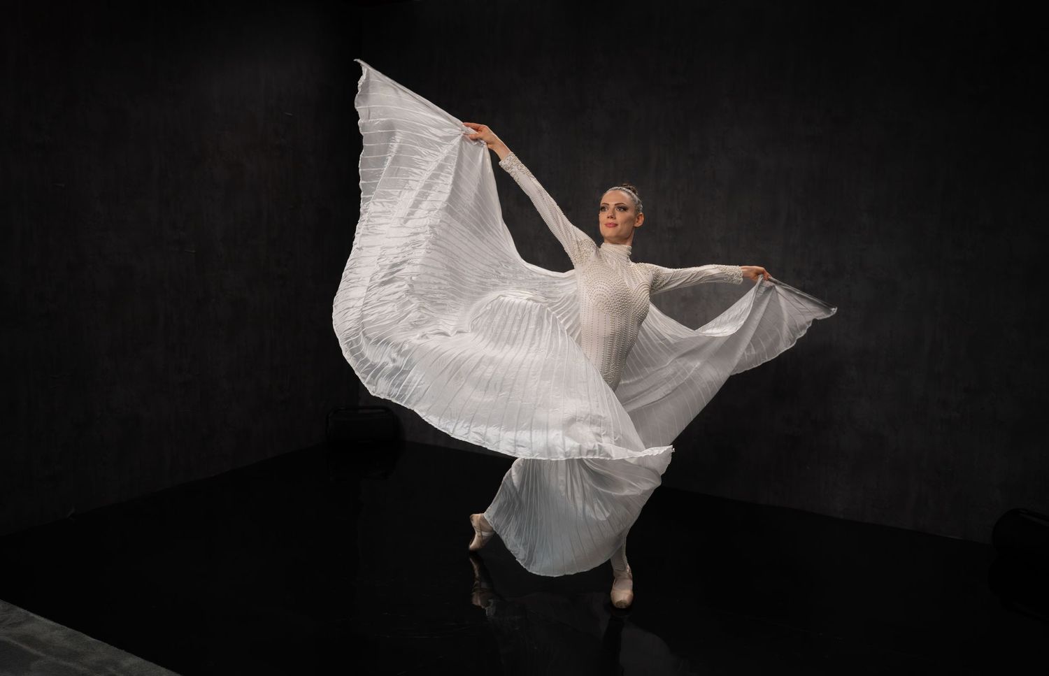 Dancer in white dress creating dramatic movement against dark backdrop.
