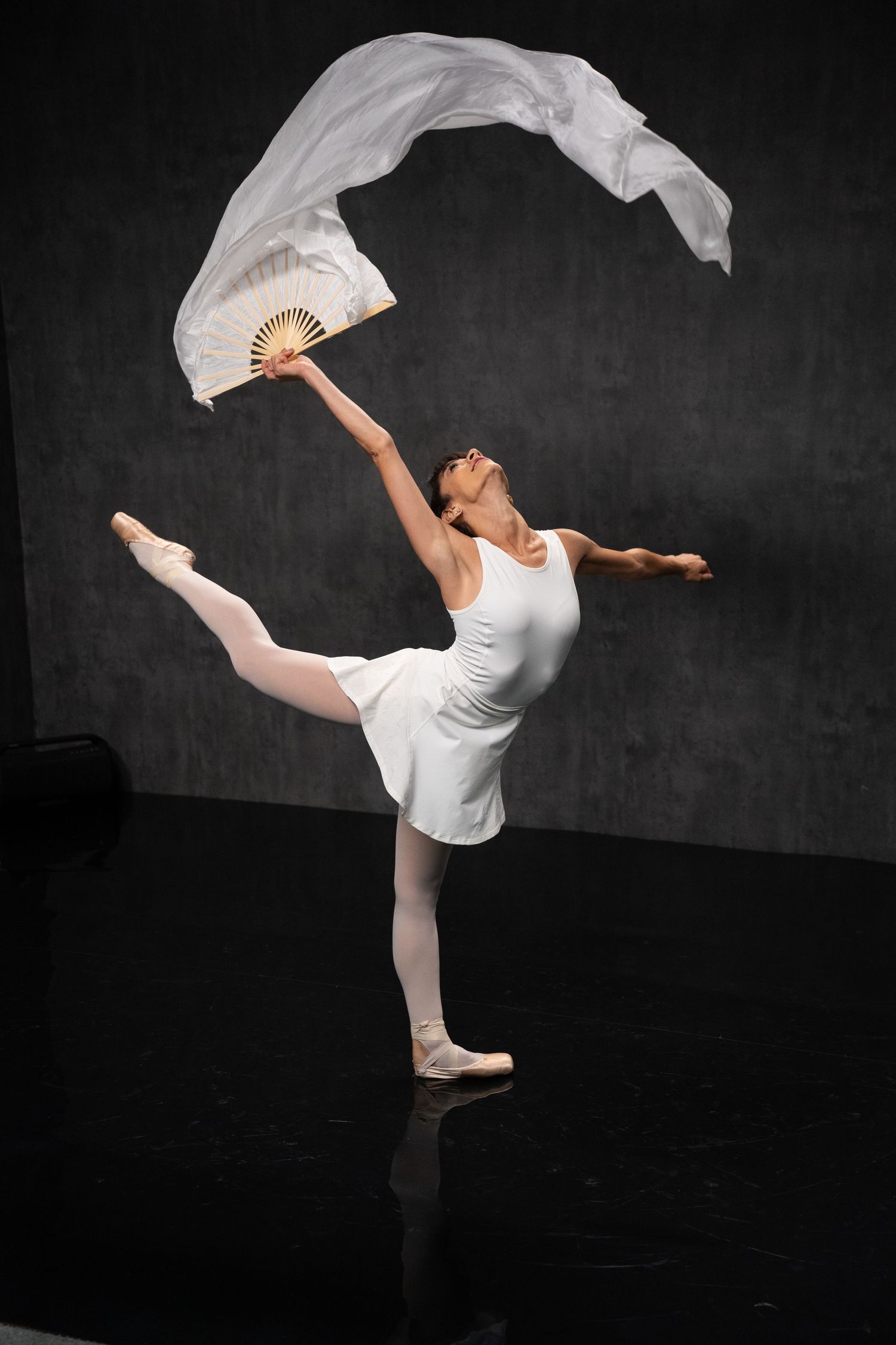Dancer performs dynamic pose with flowing white fabric against dramatic dark backdrop.